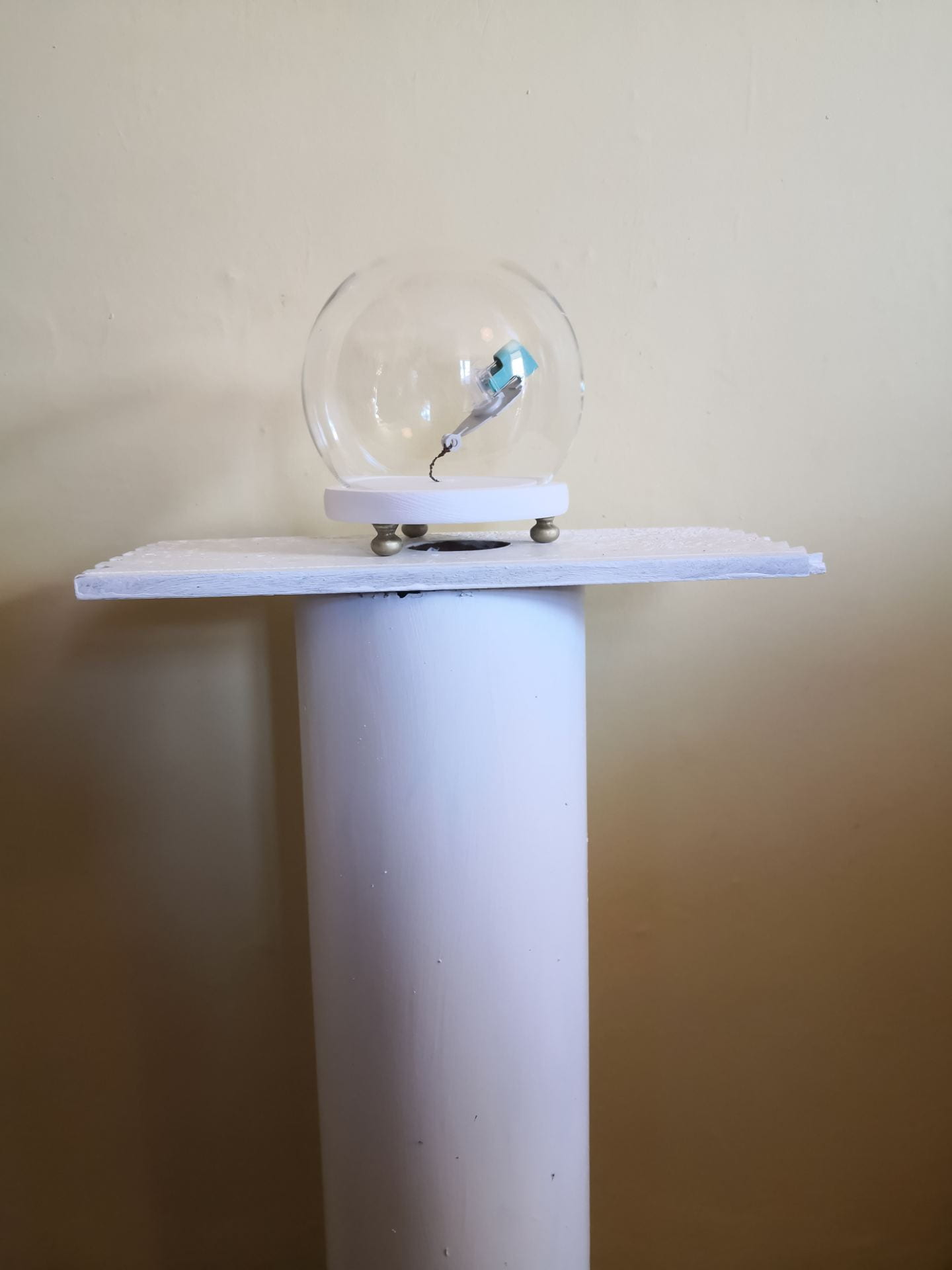 A glass bubble containing a blue fragment of an inhaler, sat on a white plinth